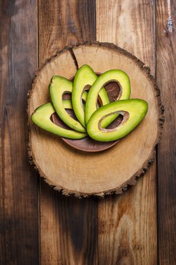 Kahverengi ahşap bir masada dilimlenmiş yeşil avokado.