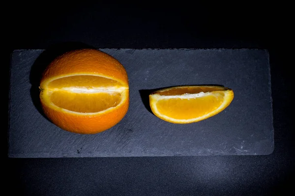 Ripe orange on a black background and black surface