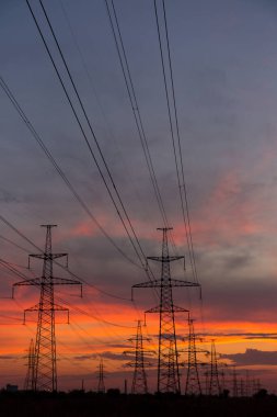 Elektrik taşımak için büyük elektrik direkleri ve güzel, turuncu, dramatik bir gün batımı.