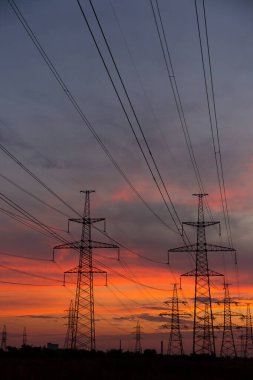 Elektrik taşımak için büyük elektrik direkleri ve güzel, turuncu, dramatik bir gün batımı.