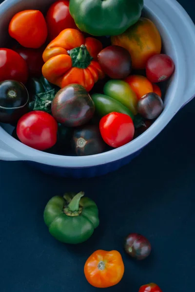 Green red orange tomatoes and green red orange peppers in white plate on black background
