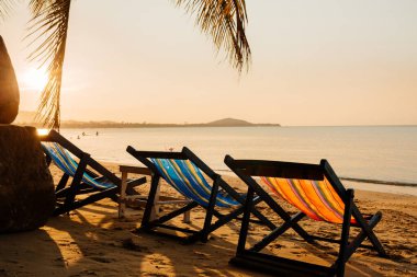 Tayland 'da tropikal bir sahilde, okyanusa ve günbatımına karşı güneşleniyorlar.