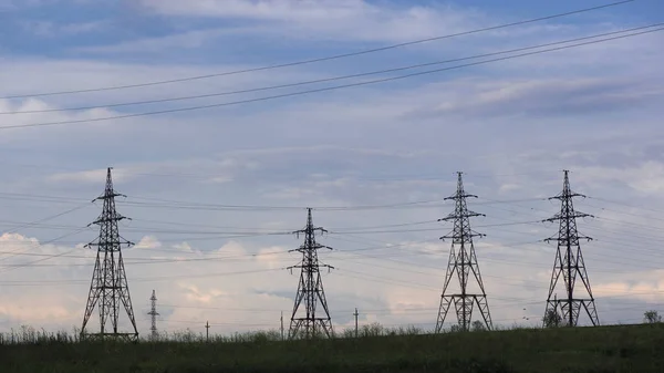 Güç hatları ve bulutlarla gökyüzü. Tarlaların üzerinden kablolar. Elektrikli dişlilerin güçlü hatları. Elektrik enerjisi endüstrisi ve doğa konsepti. Yüksek gerilim güç hatları. Saha ve hava hatları, gün batımında siluetler. Bozkırda elektrik santrali.