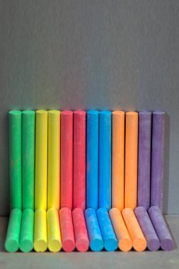 Gri bir arkaplanda renkli boyalar. Koyu arkaplanda, parlak renkli boyalar. Anaokulu çocukları için gökkuşağı renkli tebeşirli pastel..