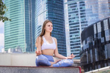 Çapraz bacaklı bina, meditasyon, meditasyon için pratik yoga kolay teşkil mavi cam modern ofis önünde oturan genç kadın