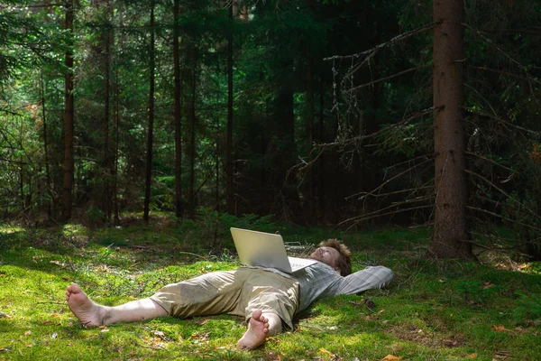 bearded hipster man lying in the forest with a notebook