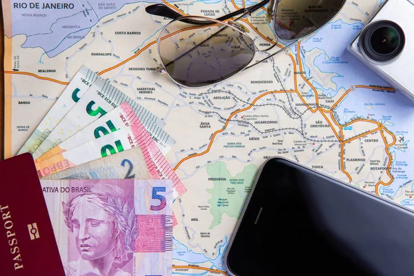 brazilian map as backround wuth passport with reais cash, mobile phone, camera and shades on the map