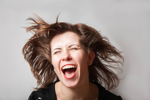 Portrait of a beautiful woman with flying hair laughing and shouting on grey background