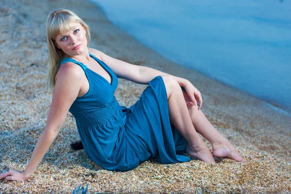 Young blond woman in long blue dress on the beach near the sea Royalty Free Stock Photos