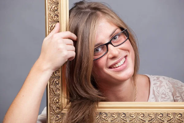 Young woman in eyeglasses looking through wooden golden frame — Stock Photo, Image