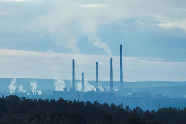 refinery with smoke stacks in a distance and forest in foregroun