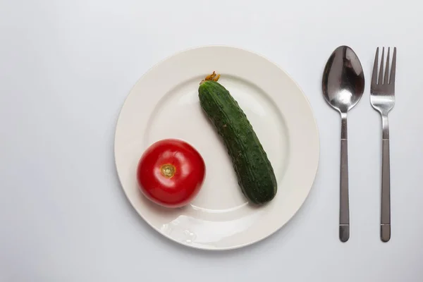 Pomidor i ogórek na talerzu w środku, sztućce na białym — Zdjęcie stockowe