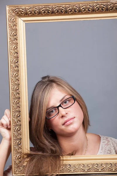 Young woman in eyeglasses looking through wooden golden frame — Stock Photo, Image