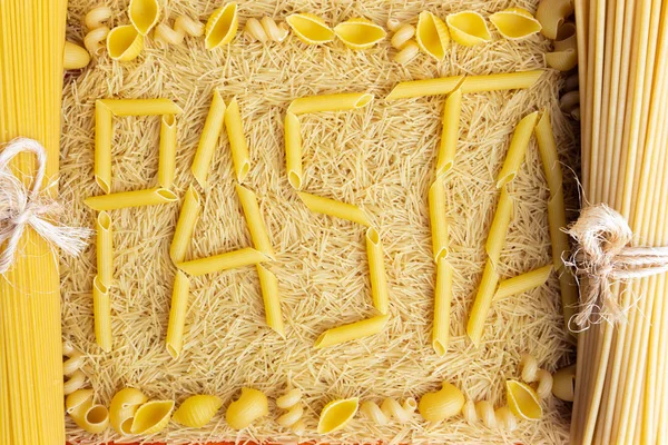 Word pasta made from penne rigate on the fone of vermicelli — стоковое фото