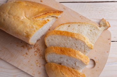 Beyaz ahşap arka plan üzerinde kesme tahtası üzerinde ekmek dilimlenmiş.