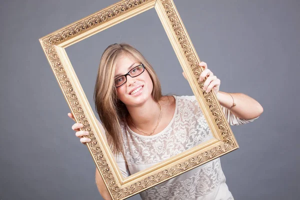 Young woman in eyeglasses looking through wooden golden frame — Stock Photo, Image