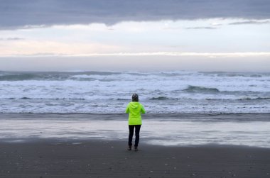 Ocean Shores, Washington'da fırtınalı bir kum plajda gün batımında yürüyen elektrikli rüzgarlık yürüyüşçü