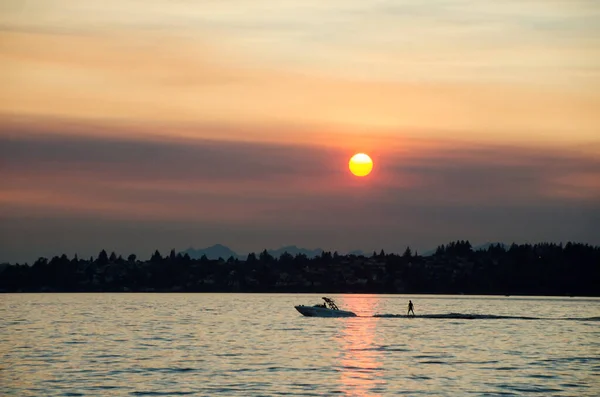 Washington Gölü 'nde sürat teknesi ve su kayakçısı. Kırmızı günbatımında bazı yangınlardan kaynaklanıyor. Arka planda Kuzeydoğu Seattle silueti var.