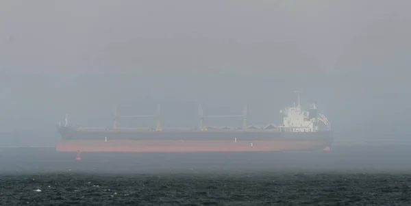 Red cargo ship hiding in dense fog while anchored near Chehalis Point in Westport, Grays Harbor, Washington