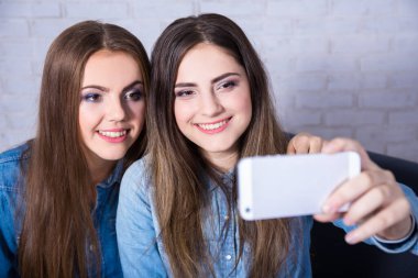 İki güzel kadın akıllı telefonlarıyla selfie çekiyorlar.