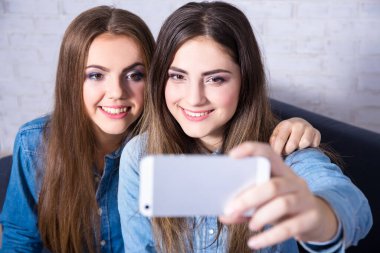 İki çekici kadın akıllı telefonlarıyla selfie çekiyorlar.