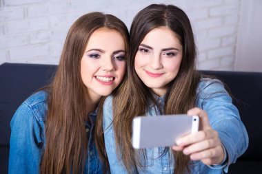 İki kız evde akıllı telefonlarıyla selfie çekiyor.