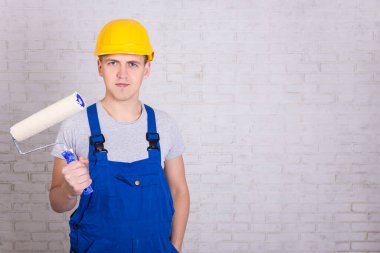 Beyaz tuğla duvarın üzerinde paten fırçası olan genç bir boyacı.