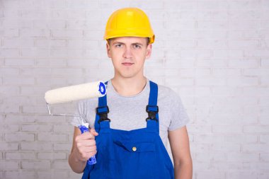 Beyaz tuğla duvarın üzerinde paten fırçası olan bir erkek ressamın portresi