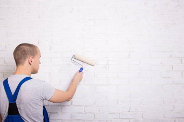 İş yerindeki genç ressamın arka plan görüntüsü beyaz tuğla duvar boyası ve boya silindiri ve kopyalama alanı