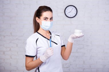 Ofisteki beyaz tuğla duvarda diş modelini ve aletleri tutan dişçi kadının portresi.