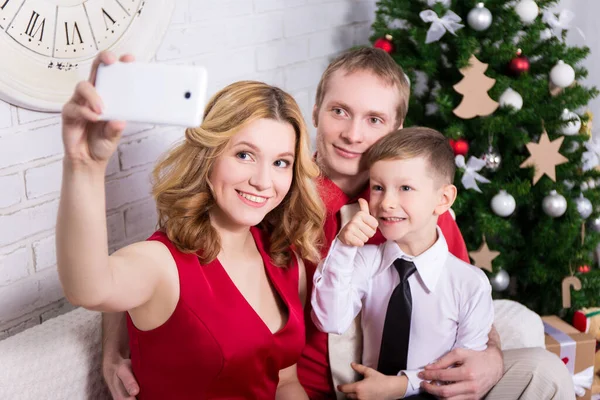 年轻的家庭在圣诞树前拿着智能手机自拍 — 图库照片