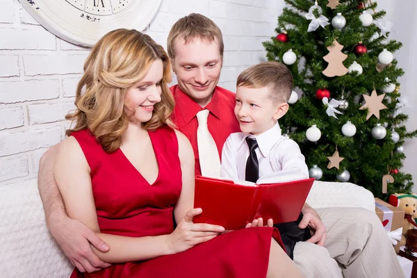 快乐的年轻家庭在圣诞树前看书 — 图库照片