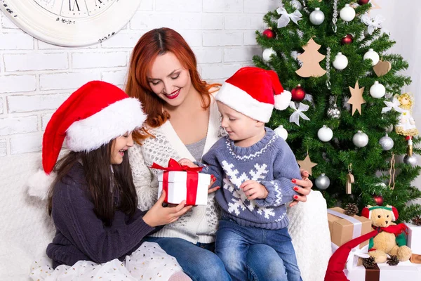 若い母親はクリスマスツリーの前で子供たちにプレゼントをし — ストック写真