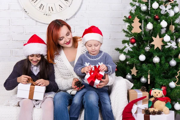 クリスマスツリーの前にギフトボックスを持つ若い幸せな母親と小さな子供たち — ストック写真