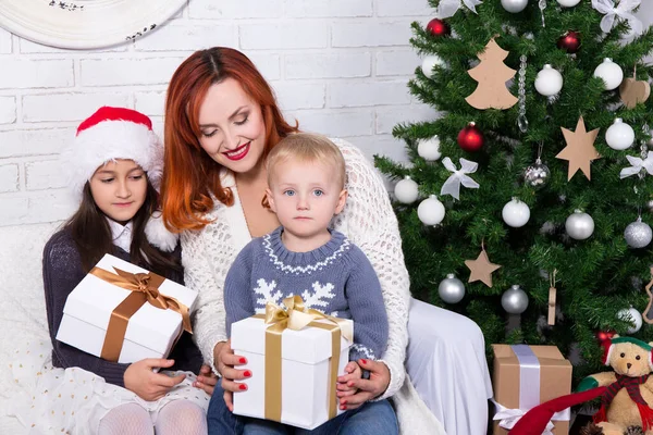 クリスマスツリーの前にギフトボックスを開く若い母親と小さな子供たち — ストック写真