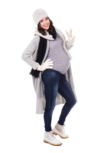 白地に隔離された勝利の印を示す冬服の若い妊婦 — ストック写真