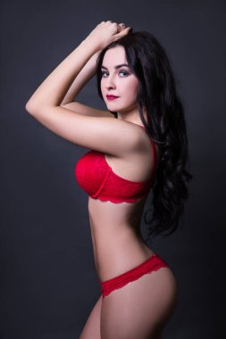 Siyah arka planda poz veren kırmızı dantel iç çamaşırlı güzel bir kadın.