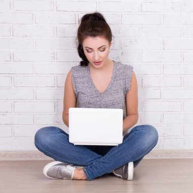 Güzel bir kadın beyaz laptopuyla yerde oturuyor.