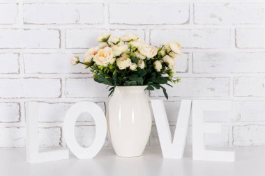 Gül çiçekleri ve beyaz ahşap kelime aşk, beyaz tuğla duvar arka planında