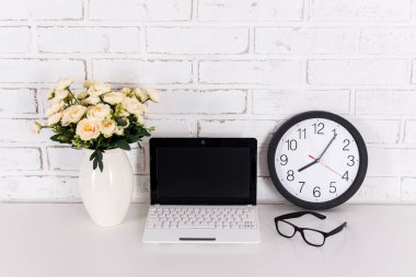 İş yeri - boş ekranlı modern dizüstü bilgisayar, ofis saati, evde veya ofiste bardak ve çiçekler