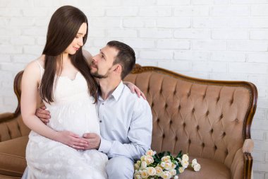 Aşk ve ebeveynlik kavramı. Evdeki klasik koltukta oturan genç, güzel, hamile bir çift.