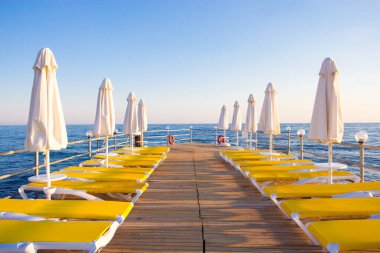 seyahat ve tatil konsepti - mavi denizde sandalyeli ve şemsiyeli ahşap iskele