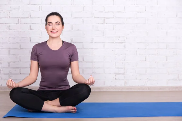 Smal Sportig Kvinna Sittande Yogapose Blå Matta Över Vit Tegelvägg — Stockfoto