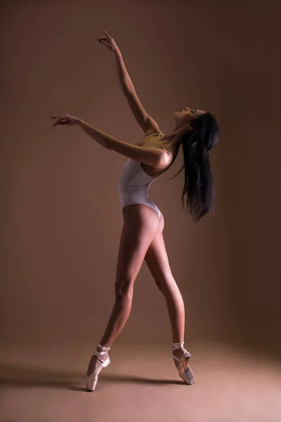 young beautiful woman ballet dancer posing on toes over beige background