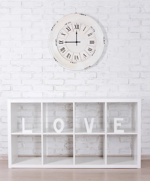木製の手紙形成単語愛で現代的な棚とヴィンテージ時計上の白いレンガの壁 — ストック写真
