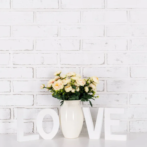 Gül çiçekleri ve ahşap harfler Beyaz tuğla duvarın üzerinde aşk