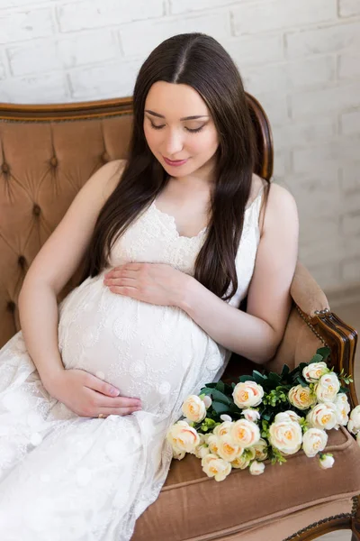 幸せな若い美しい妊娠中の女性の肖像 自宅で花とヴィンテージソファに座って — ストック写真
