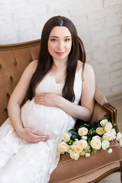 快乐的年轻美丽的孕妇坐在长满玫瑰花的老式沙发上 — 图库照片