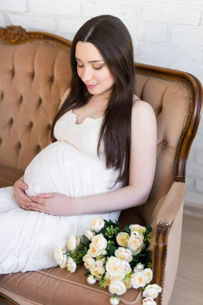 幸せな若いです美しいです妊娠中の女性で白のドレス座っている上のヴィンテージソファ — ストック写真