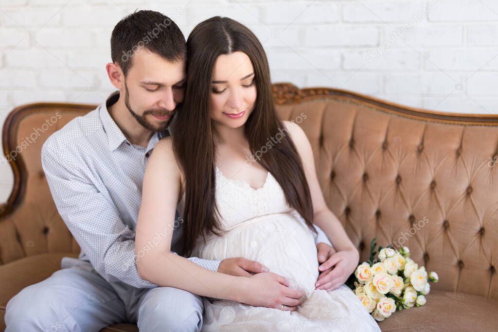 young pregnant woman with husband sitting on vintage sofa at home